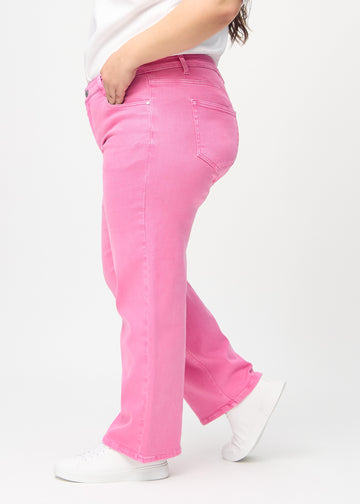 Loose-jeans til kvinner i lyserosa, fargen Flamingos. Sett fra siden på en plus size-modell, med synlig løs passform.