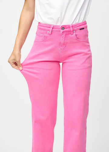 Loose-jeans til kvinner i lyserosa, fargen Flamingos. En modell strekker jeansstoffet ved låret for å vise stretchen.