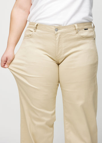 Loose-jeans til kvinner i beige, fargen Gazelles. En plus size-modell strekker jeansstoffet ved låret for å vise stretchen.