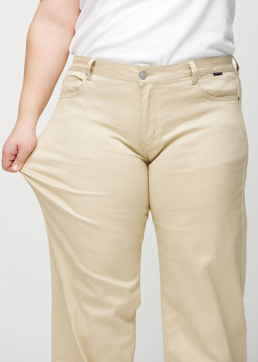 Loose-jeans til kvinner i beige, fargen Gazelles. En plus size-modell strekker jeansstoffet ved låret for å vise stretchen.