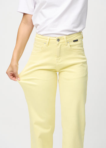 Loose-jeans til kvinner i lysegul, fargen Lemonades. En modell strekker jeansstoffet ved låret for å vise stretchen.