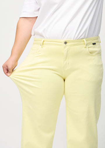Loose-jeans til kvinner i lysegul, fargen Lemonades. En plus size-modell strekker jeansstoffet ved låret for å vise stretchen.