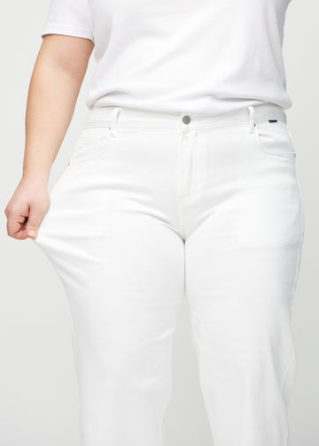 Loose-jeans til kvinner i hvit, fargen Marguerites. En plus size-modell strekker jeansstoffet ved låret for å vise stretchen.