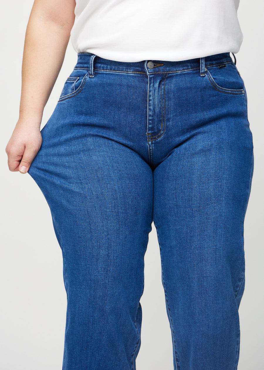 Loose-jeans til kvinner i mørkeblå, fargen Oceans. En plus size-modell strekker jeansstoffet ved låret for å vise stretchen.