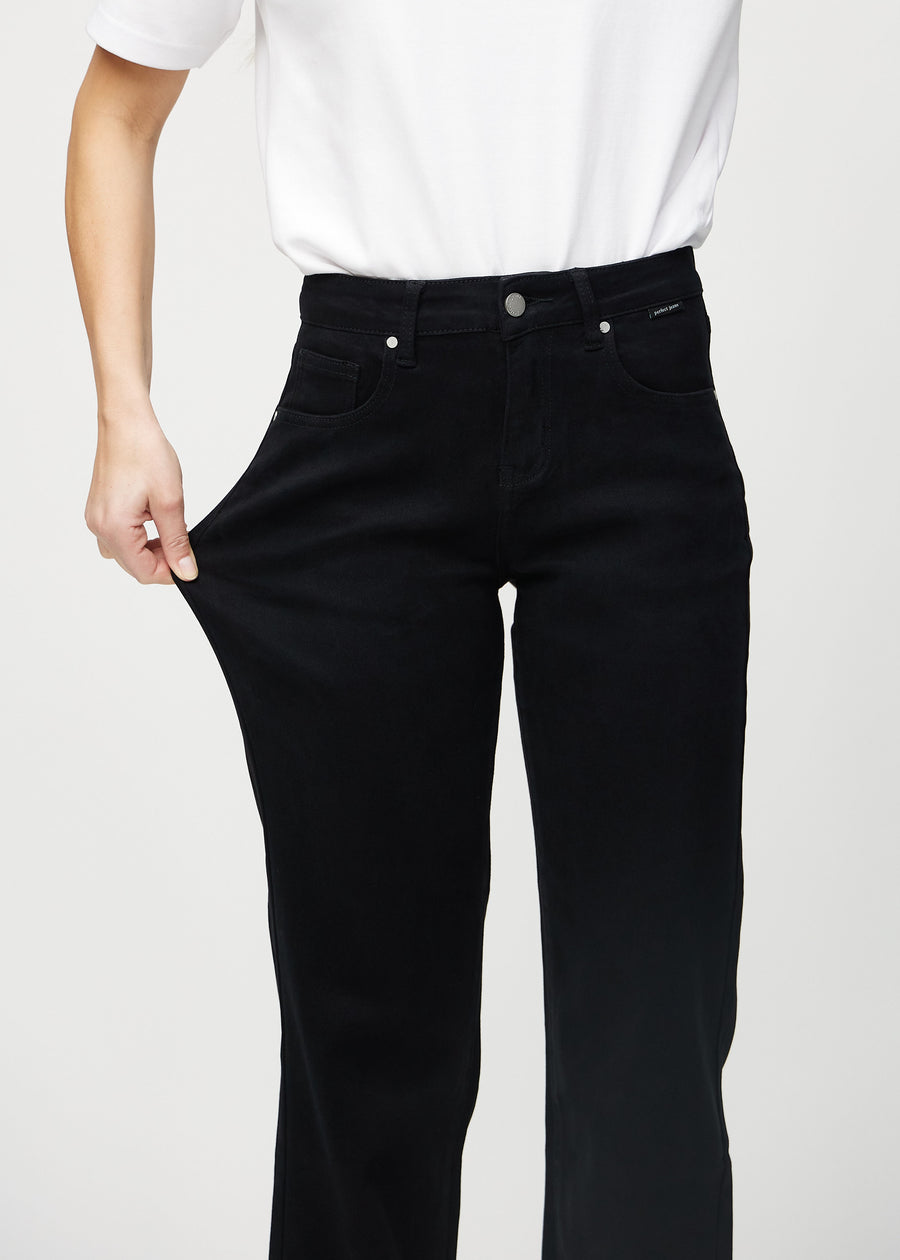 Loose-jeans til kvinner i sort, fargen Ravens. En modell strekker jeansstoffet ved låret for å vise stretchen.