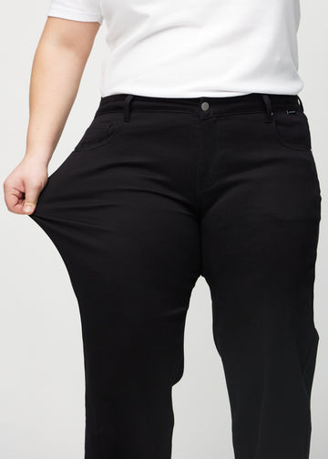 Loose-jeans til kvinner i sort, fargen Ravens. En plus size-modell strekker jeansstoffet ved låret for å vise stretchen.