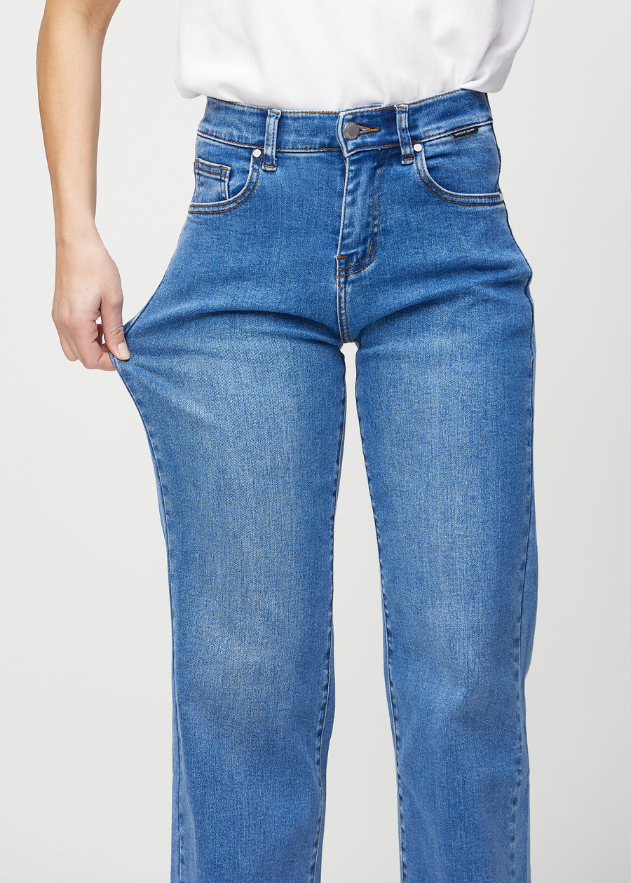 Loose-jeans til kvinner i blå, fargen Rivers. En modell strekker jeansstoffet ved låret for å vise stretchen.
