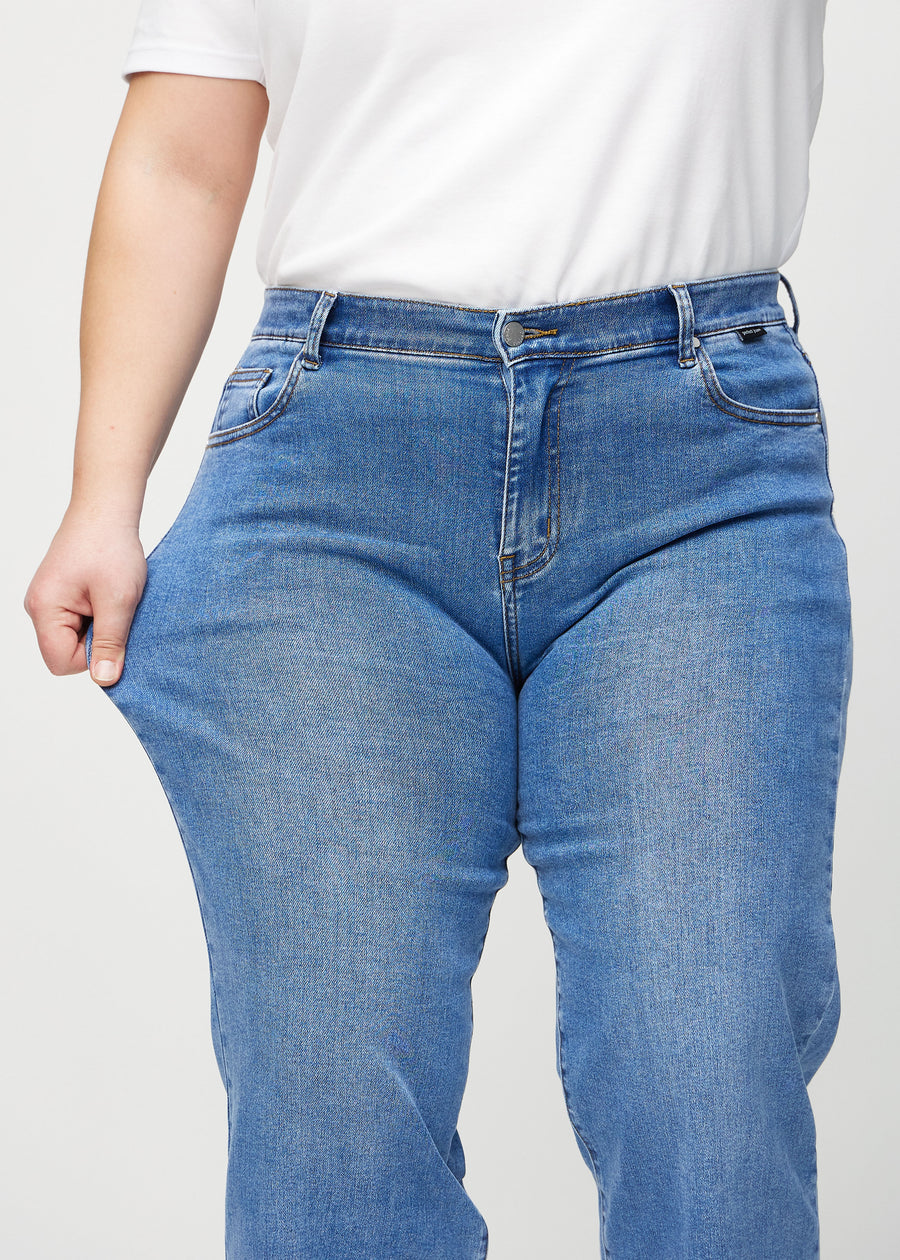 Loose-jeans til kvinner i blå, fargen Rivers. En plus size-modell strekker jeansstoffet ved låret for å vise stretchen.