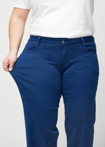 Loose-jeans til kvinner i mørkeblå, fargen Royals. En plus size-modell strekker jeansstoffet ved låret for å vise stretchen.