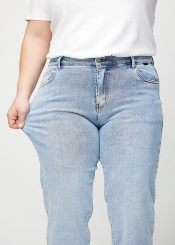 Loose-jeans til kvinner i lyseblå, fargen Waves. En plus size-modell strekker jeansstoffet ved låret for å vise stretchen.