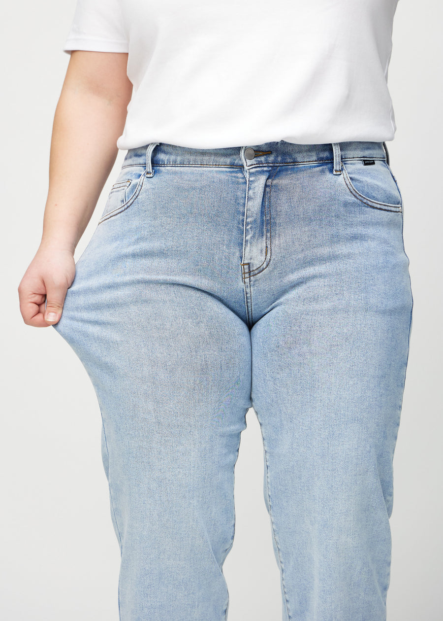 Loose-jeans til kvinner i lyseblå, fargen Waves. En plus size-modell strekker jeansstoffet ved låret for å vise stretchen.