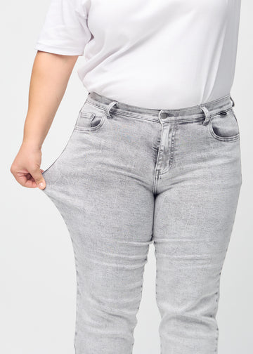 Regular-jeans til kvinner i lysegrå, fargen Ashes. En plus size-modell strekker stoffet ved låret for å vise stretchen.
