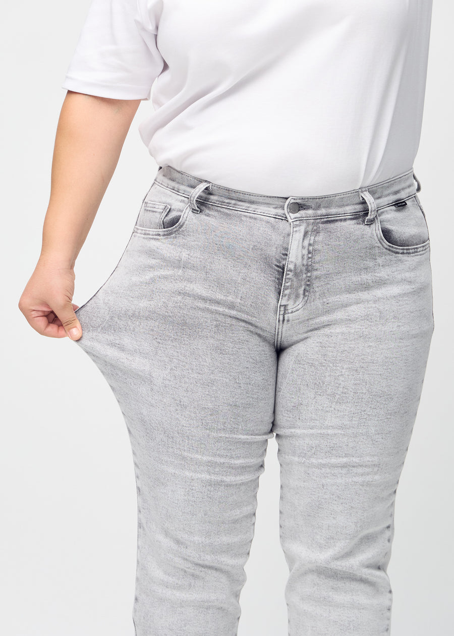 Regular-jeans til kvinner i lysegrå, fargen Ashes. En plus size-modell strekker stoffet ved låret for å vise stretchen.