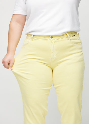 Regular-jeans til kvinner i lysegul, fargen Lemonades. En plus size-modell strekker stoffet ved låret for å vise stretchen.