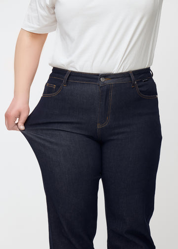 Plus-size-modell strekker dyp mørkeblå denim jeans til kvinner i fargen Midnights ved låret for å vise materialets stretch.