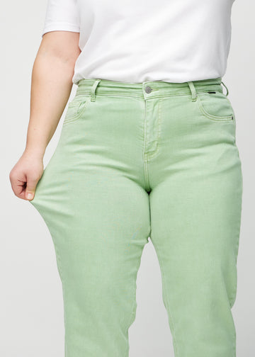 Regular-jeans til kvinner i lysegrønn, fargen Mints. En plus size-modell strekker stoffet ved låret for å vise stretchen.