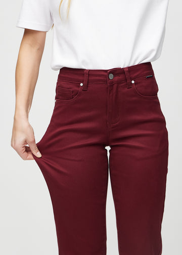 Regular-jeans til kvinner i mørkerød, fargen Santas. En modell strekker stoffet ved låret for å vise stretchen.