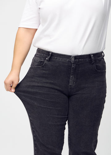 Regular-jeans til kvinner i mørkegrå, fargen Shadows. En plus size-modell strekker stoffet ved låret for å vise stretchen.