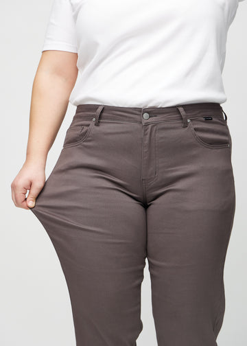 Regular-jeans til kvinner i gråbrun, fargen Thunders. En plus size-modell strekker stoffet ved låret for å vise stretchen.