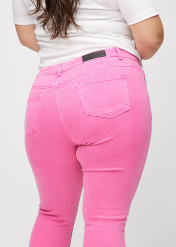 Skinny-jeans til kvinner i lyserosa, fargen Flamingos. Nærbilde bakfra på en plus size-modell for å vise detaljer.