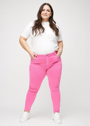 Skinny-jeans til kvinner i lyserosa, fargen Flamingos. Helhetsbilde av en plus size-modell med jeansene på.