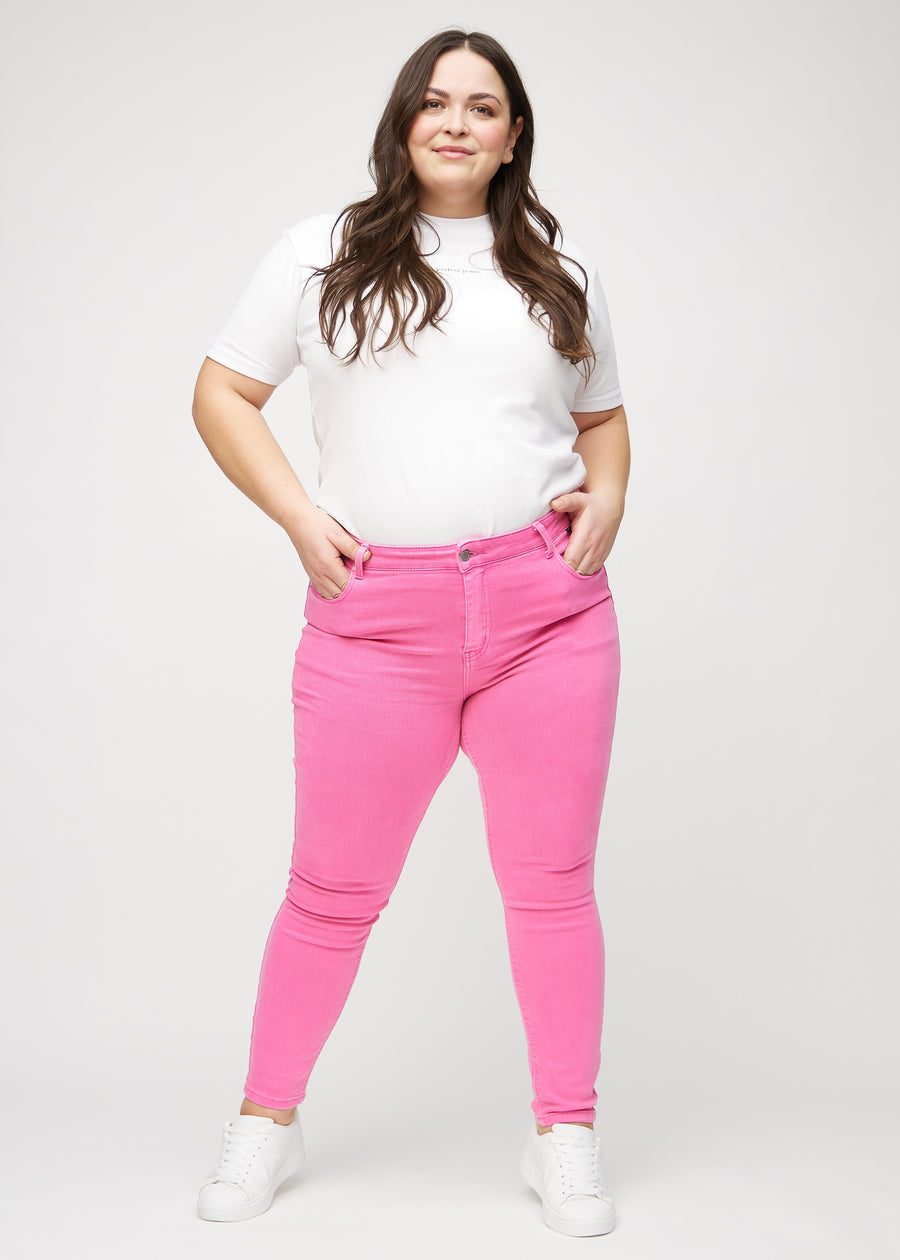 Skinny-jeans til kvinner i lyserosa, fargen Flamingos. Helhetsbilde av en plus size-modell med jeansene på.