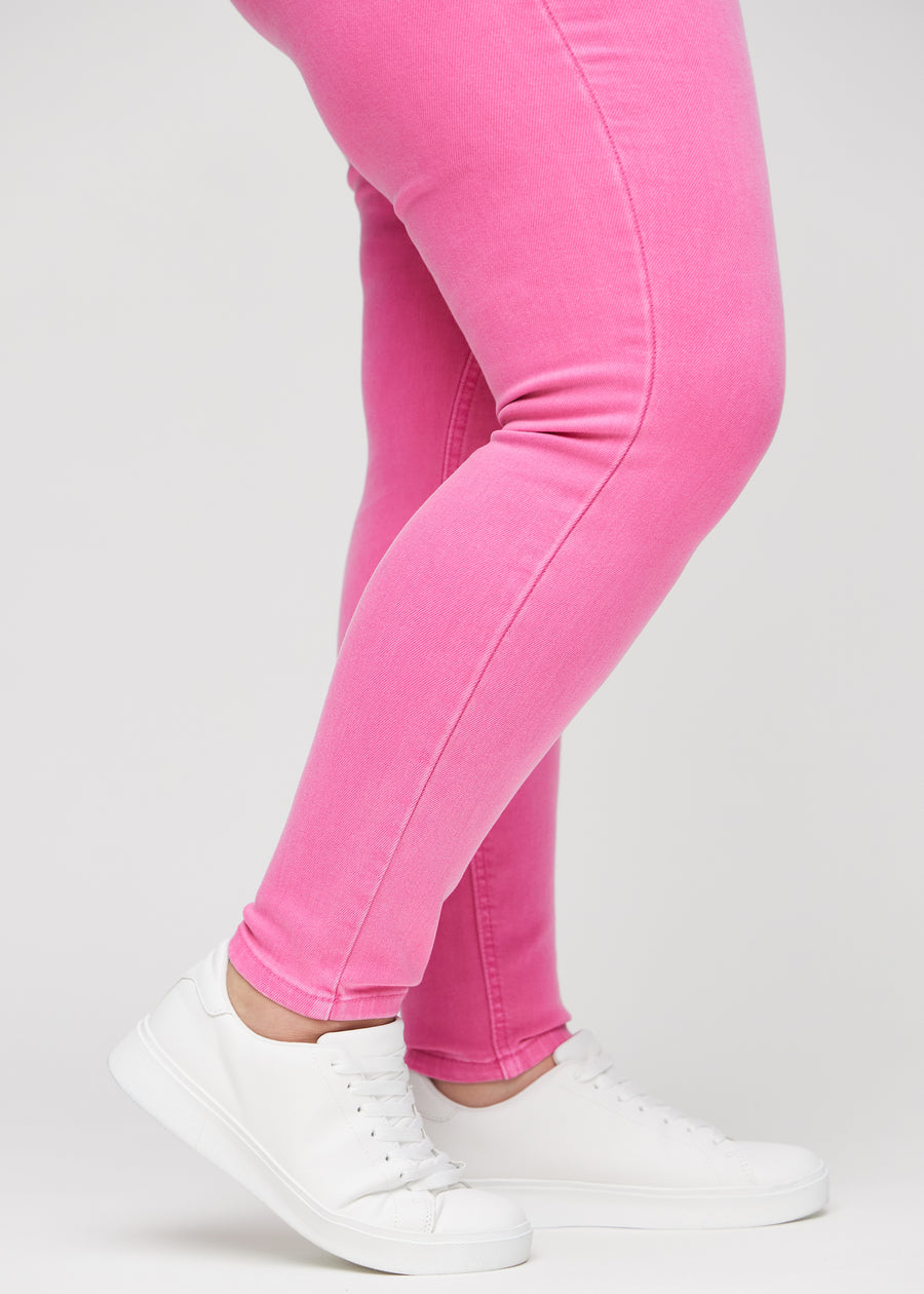 Skinny-jeans til kvinner i lyserosa, fargen Flamingos. Nærbilde ved anklene på en plus size-modell, som viser de tettsittende benåpningene.