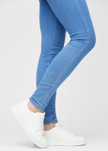Skinny-jeans til kvinner i blå, fargen Geraniums. Nærbilde ved anklene på en modell, som viser de tettsittende benåpningene.