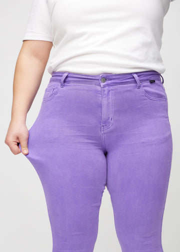 Skinny-jeans til kvinner i lilla, fargen Lavenders. En plus size-modell strekker jeansstoffet ved låret for å vise stretchen.