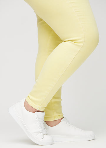 Skinny-jeans til kvinner i lysegul, fargen Lemonades. Nærbilde ved anklene på en plus size-modell, som viser de tettsittende benåpningene.