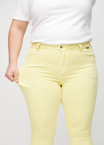 Skinny-jeans til kvinner i lysegul, fargen Lemonades. En plus size-modell strekker jeansstoffet ved låret for å vise stretchen.