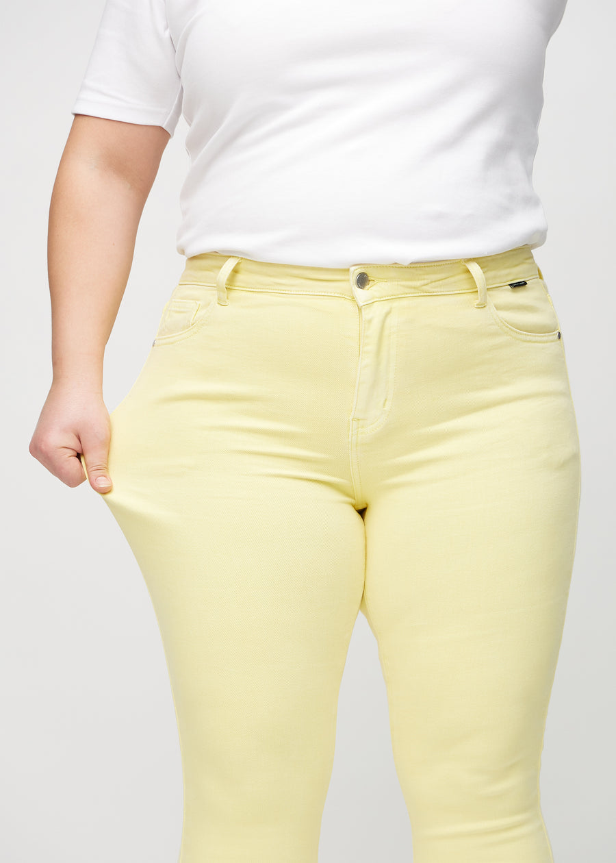 Skinny-jeans til kvinner i lysegul, fargen Lemonades. En plus size-modell strekker jeansstoffet ved låret for å vise stretchen.