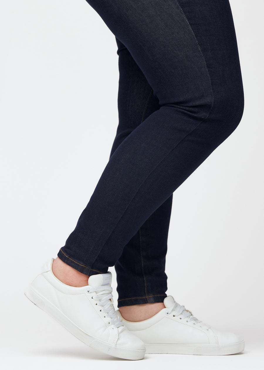 Dyp mørkeblå denim jeans til kvinner i fargen Midnights med skinny passform sett på nært hold ved anklene på plus-size-modell for å vise den tettsittende avslutningen.