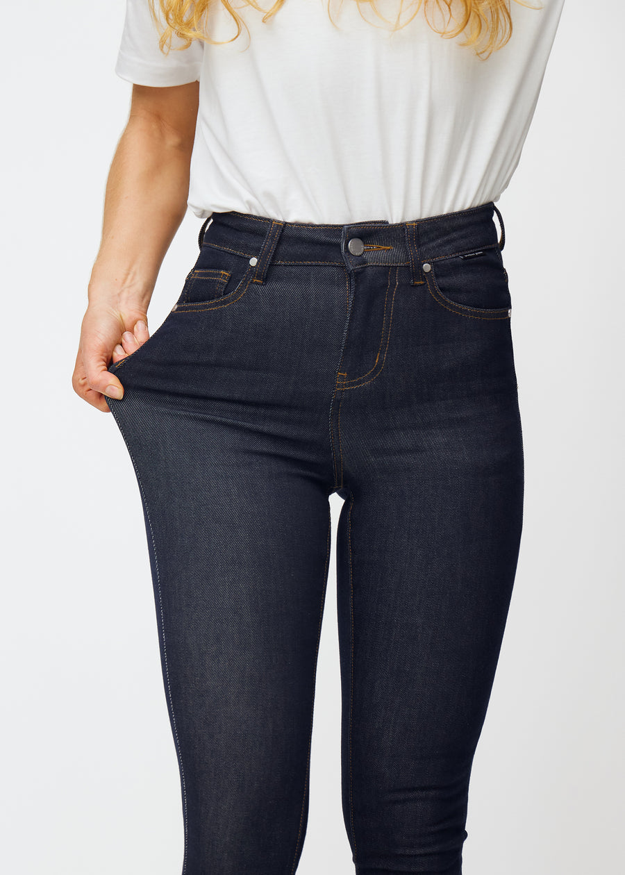 Modell strekker dyp mørkeblå denim jeans til kvinner i fargen Midnights ved låret for å vise materialets stretch.