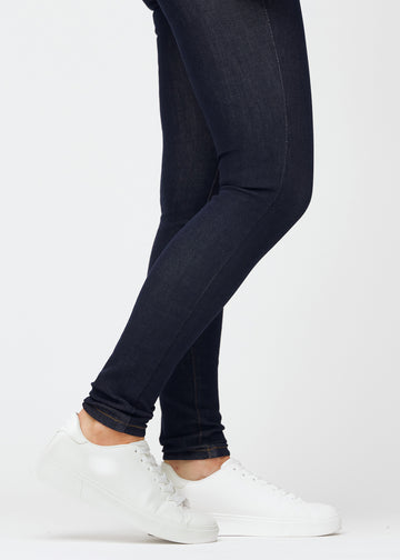 Dyp mørkeblå denim jeans til kvinner i fargen Midnights med skinny passform sett på nært hold ved anklene for å vise den tettsittende avslutningen.
