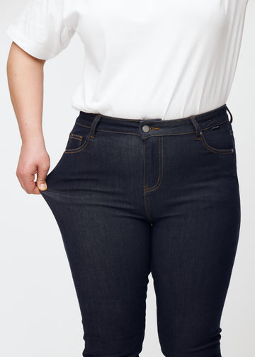 Plus-size-modell strekker dyp mørkeblå denim jeans til kvinner i fargen Midnights ved låret for å vise materialets stretch.