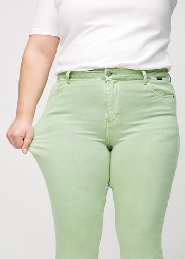 Skinny-jeans til kvinner i lysegrønn, fargen Mints. En plus size-modell strekker jeansstoffet ved låret for å vise stretchen.