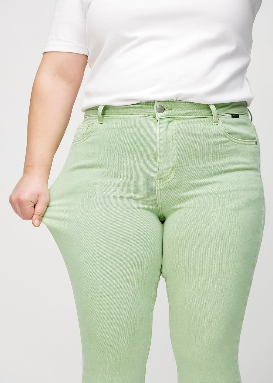 Skinny-jeans til kvinner i lysegrønn, fargen Mints. En plus size-modell strekker jeansstoffet ved låret for å vise stretchen.