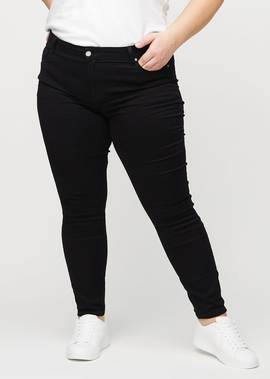 Svarte skinny jeans, modellnavn Ravens, som sitter tett på benet på en plus-size-modell, sett forfra.