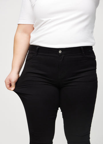 Plus-size-modellen strekker jeansene ved låret for å vise stretch.