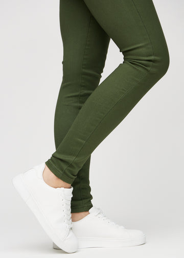 Skinny-jeans til kvinner i mørkegrønn, fargen Renewals. Nærbilde ved anklene på en modell, som viser de tettsittende benåpningene.