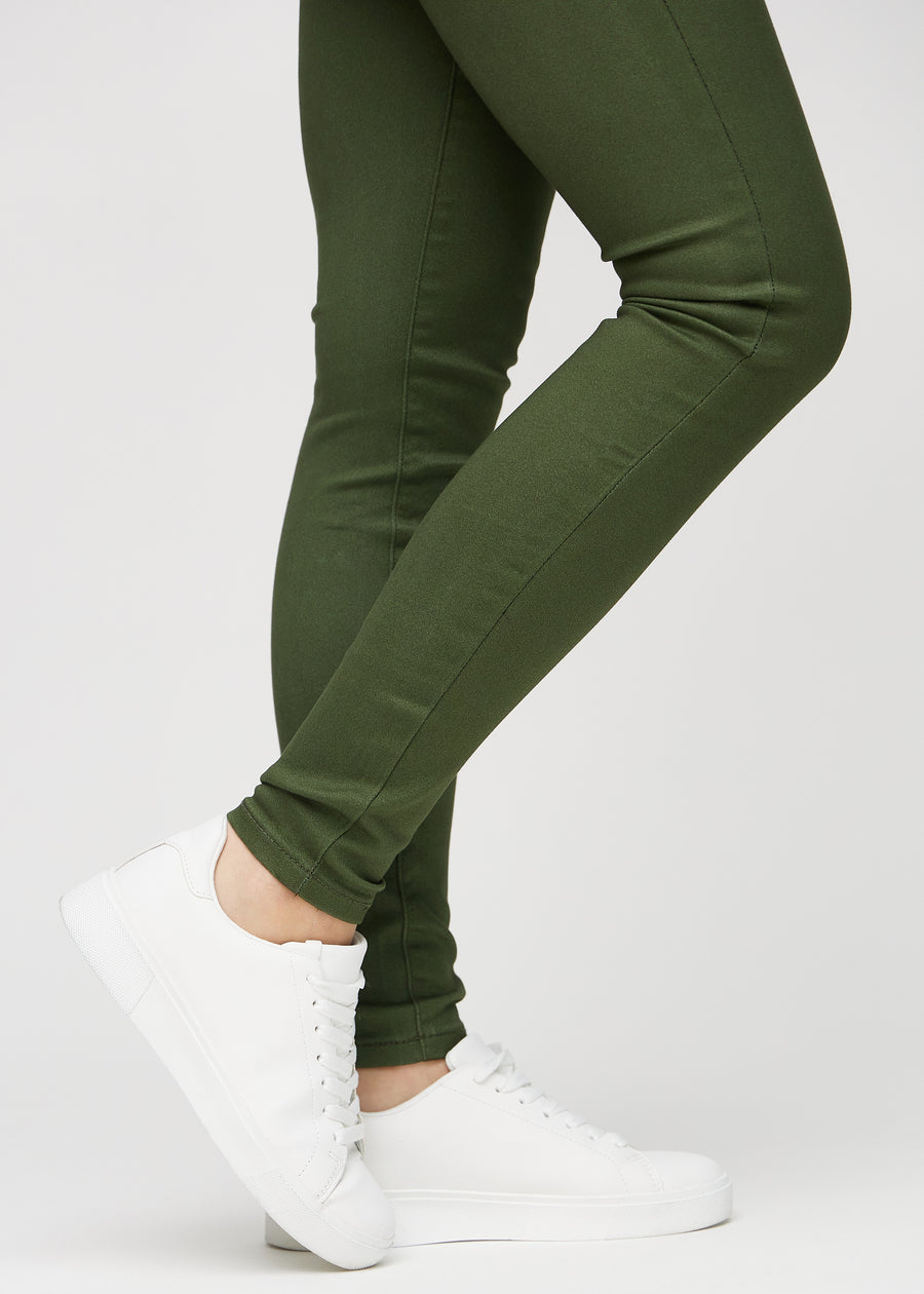 Skinny-jeans til kvinner i mørkegrønn, fargen Renewals. Nærbilde ved anklene på en modell, som viser de tettsittende benåpningene.