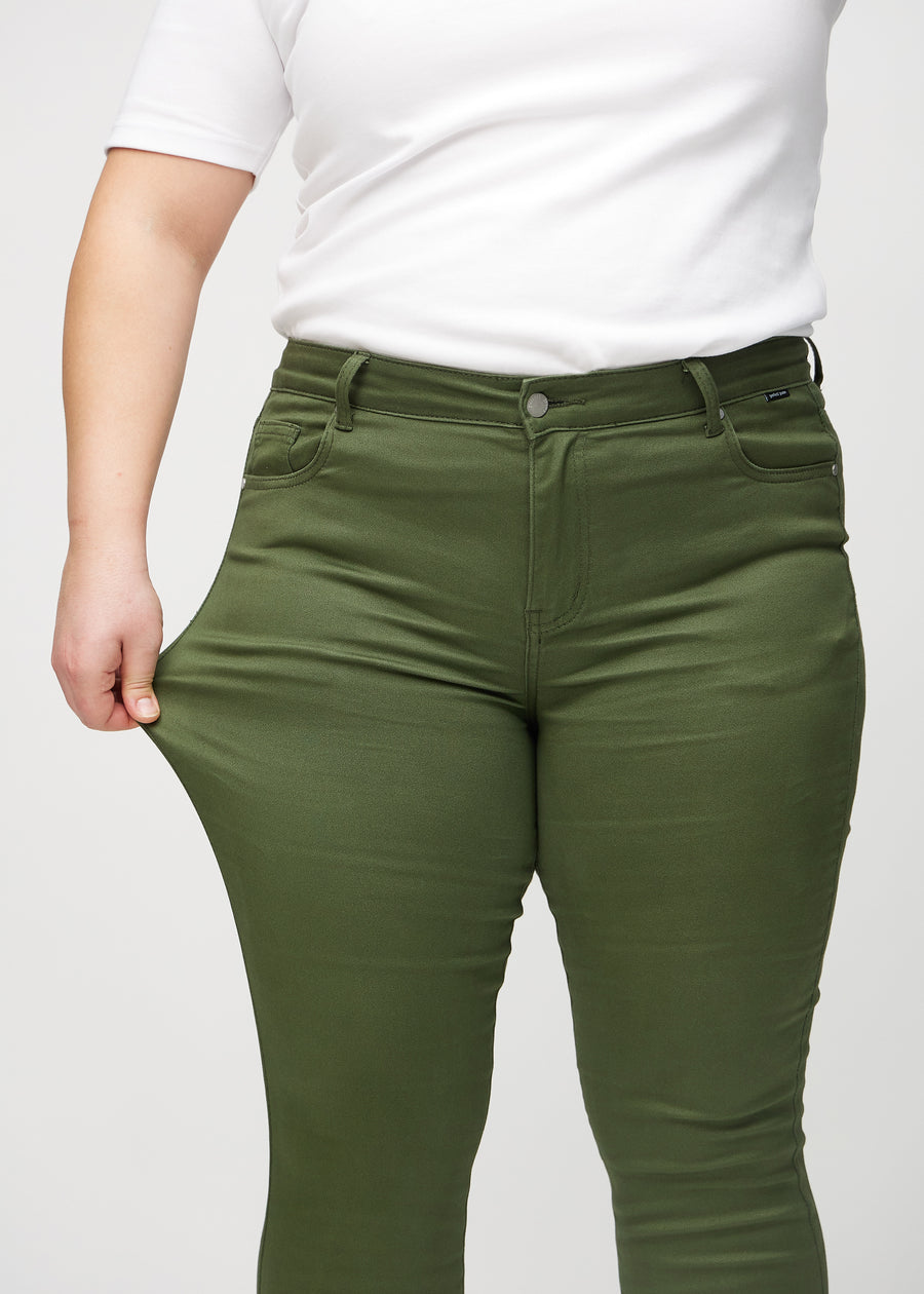 Skinny-jeans til kvinner i mørkegrønn, fargen Renewals. En plus size-modell strekker jeansstoffet ved låret for å vise stretchen.