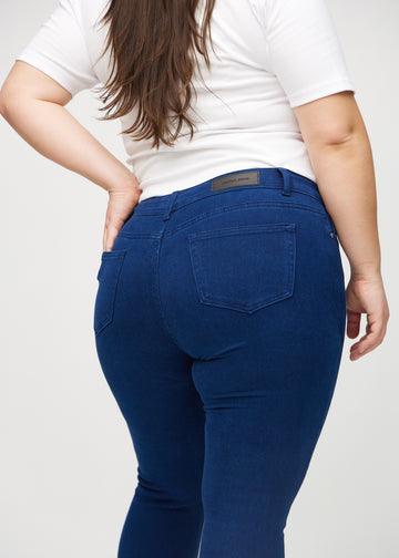 Mørkeblå skinny jeans sett bakfra på nært hold på en plus-size-modell for å vise detaljer.