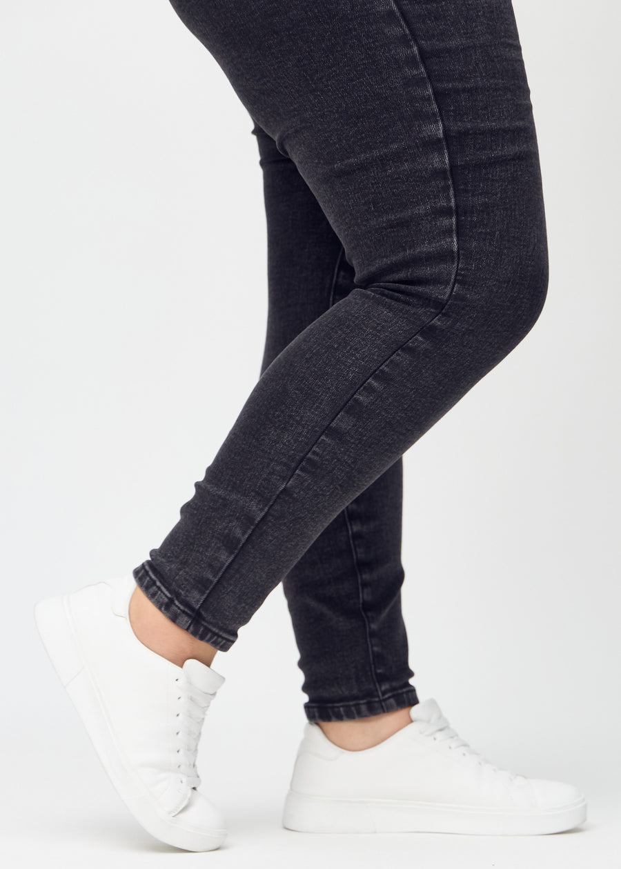 Skinny-jeans til kvinner i mørkegrå, fargen Shadows. Nærbilde ved anklene på en plus size-modell, som viser de tettsittende benåpningene.