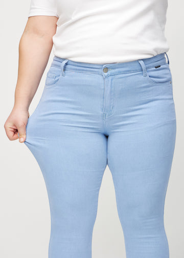 Skinny-jeans til kvinner i lyseblå, fargen Skies. En plus size-modell strekker jeansstoffet ved låret for å vise stretchen.