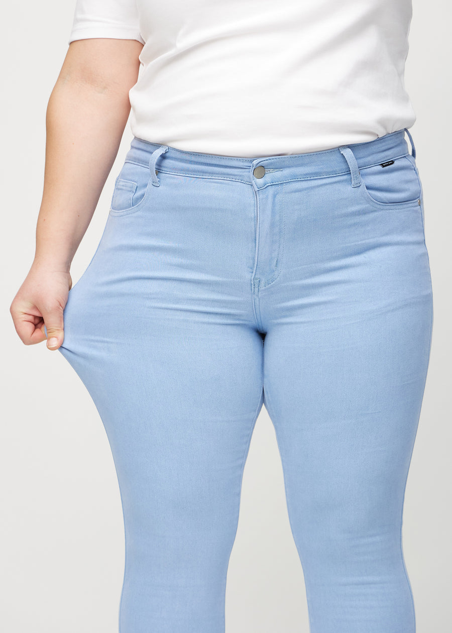 Skinny-jeans til kvinner i lyseblå, fargen Skies. En plus size-modell strekker jeansstoffet ved låret for å vise stretchen.