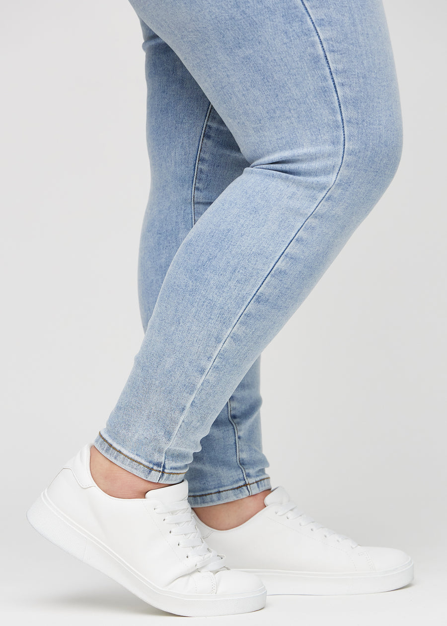 Skinny-jeans til kvinner i lyseblå, fargen Waves. Nærbilde ved anklene på en plus size-modell, som viser de tettsittende benåpningene.