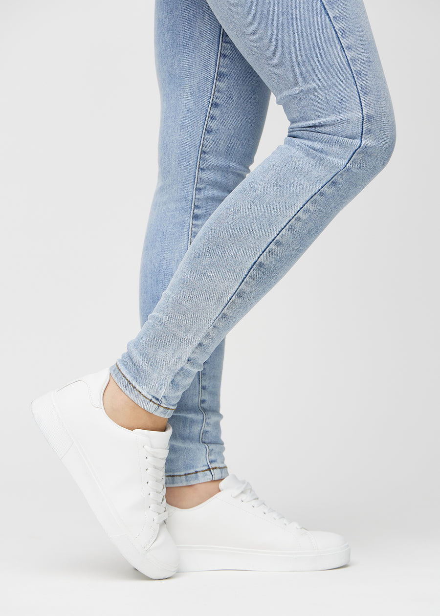 Skinny-jeans til kvinner i lyseblå, fargen Waves. Nærbilde ved anklene på en modell, som viser de tettsittende benåpningene.