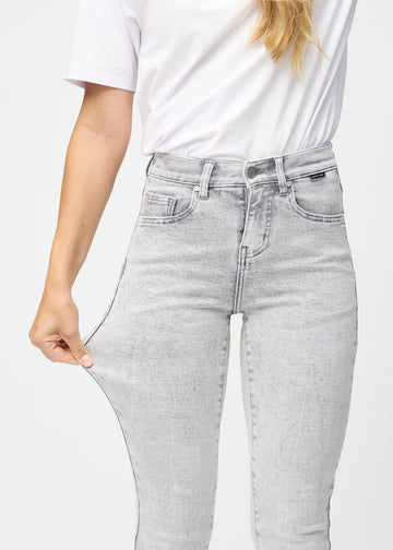 Slim-jeans til kvinner i lysegrå, fargen Ashes. En modell strekker jeansstoffet ved låret for å vise stretchen.